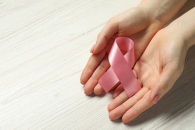 Breast cancer awareness. Woman with pink ribbon at white wooden table, closeup. Space for text
