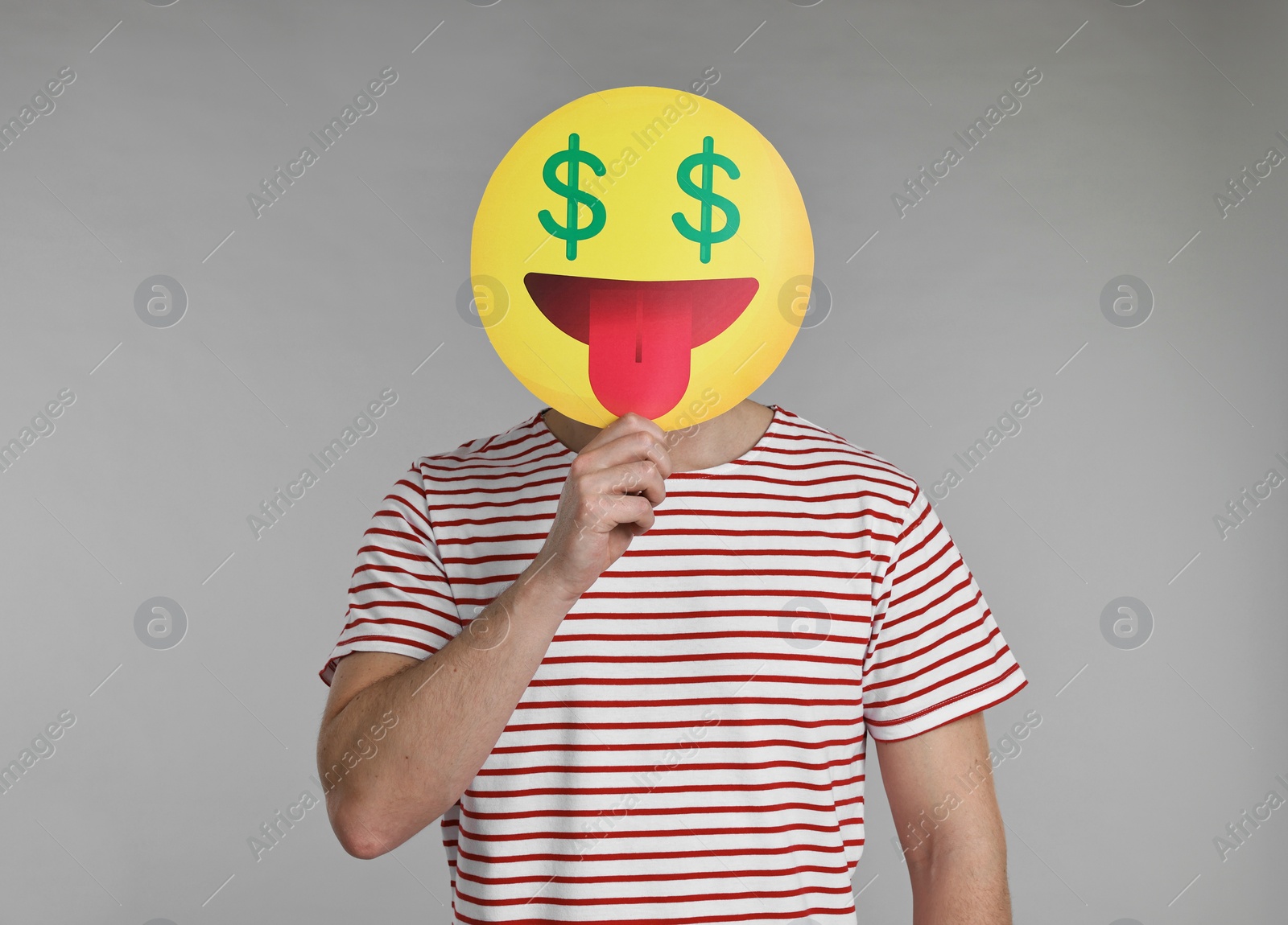 Photo of Man holding emoticon with dollar signs instead of eyes on grey background