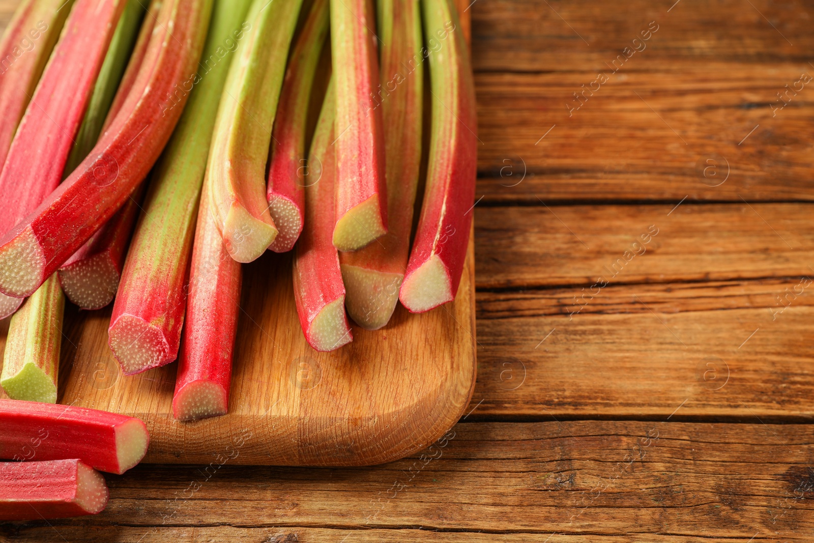 Photo of Many cut rhubarb stalks on wooden table, closeup. Space for text