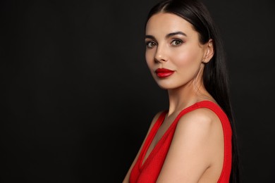Photo of Portrait of young woman wearing beautiful red lipstick on black background, space for text