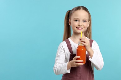 Cute little girl holding glass bottle of fresh juice with straw on light blue background, space for text