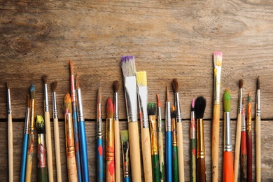 Photo of Different paint brushes on wooden background, top view with space for text