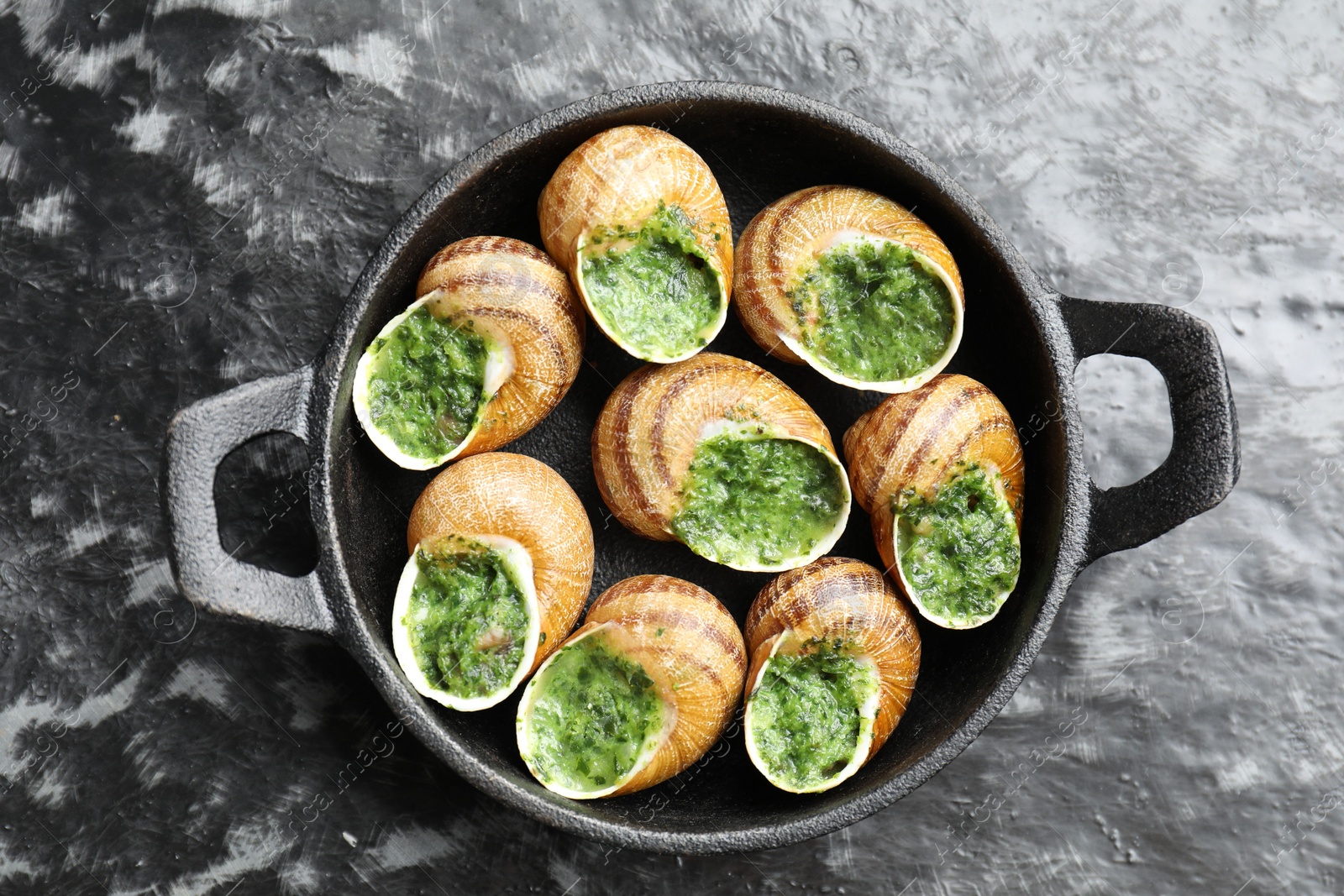 Photo of Delicious cooked snails in baking dish on grey textured table, top view