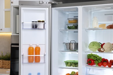 Photo of Open refrigerator full of different products in kitchen