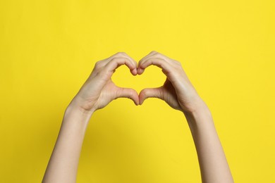 Photo of Woman making heart with her hands on yellow background, closeup