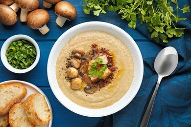 Photo of Delicious mushroom cream soup and ingredients on blue wooden table, flat lay