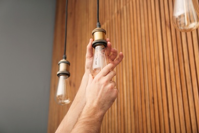 Photo of Man changing lamp light bulb indoors, closeup