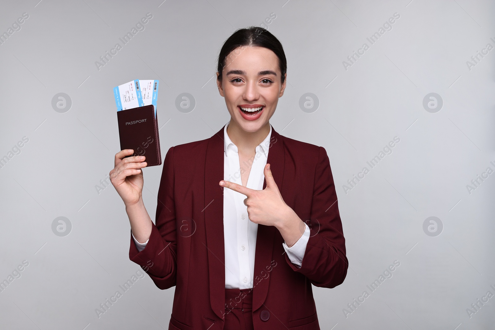 Photo of Happy businesswoman pointing at passport and tickets on grey background