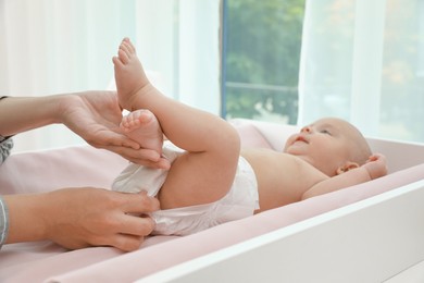 Mother changing her baby's diaper on table at home