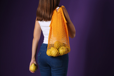 Photo of Woman holding net bag with fresh ripe pears on purple background, closeup