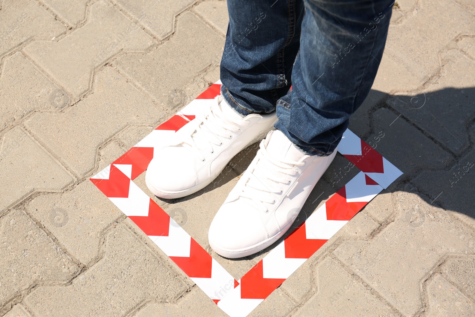 Photo of Man standing on taped floor marking for social distance outdoors, closeup. Coronavirus pandemic