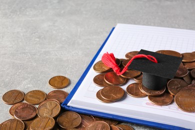 Photo of Scholarship concept. Graduation cap, notebook and coins on light grey table, closeup