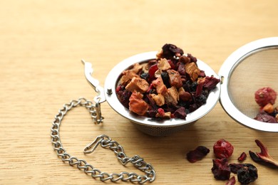 Photo of Snap infuser with dried herbal tea leaves and fruits on wooden table, closeup