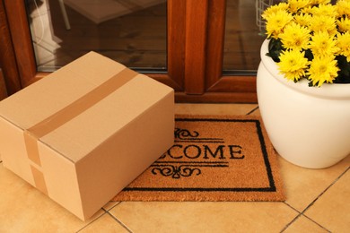 Photo of Parcel on door mat and beautiful flowers near entrance