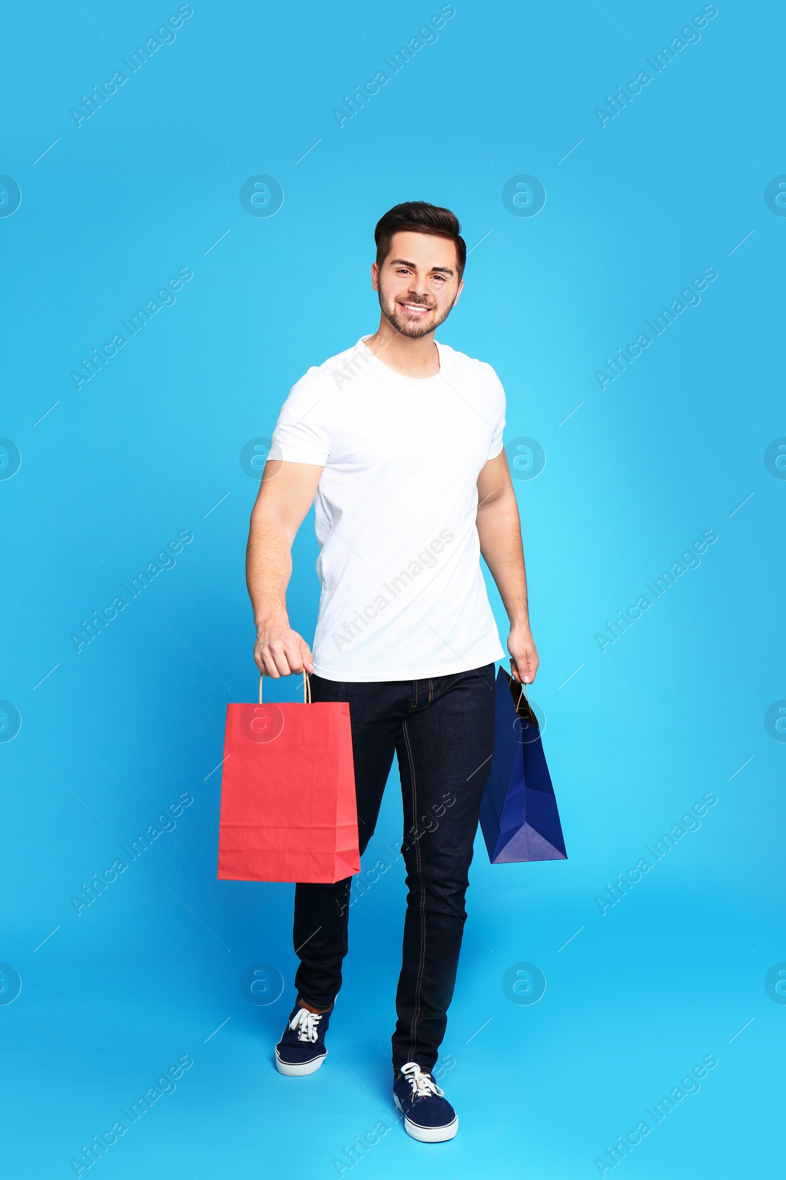 Photo of Full length portrait of young man with paper bags on blue background