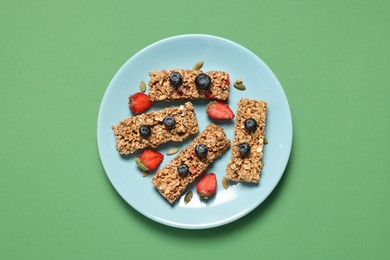 Tasty granola bars and berries on green background, top view