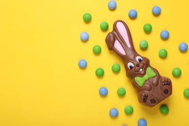 Chocolate Easter bunny and candies on yellow background, flat lay. Space for text