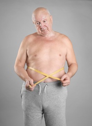 Photo of Fat senior man with measuring tape on grey background. Weight loss