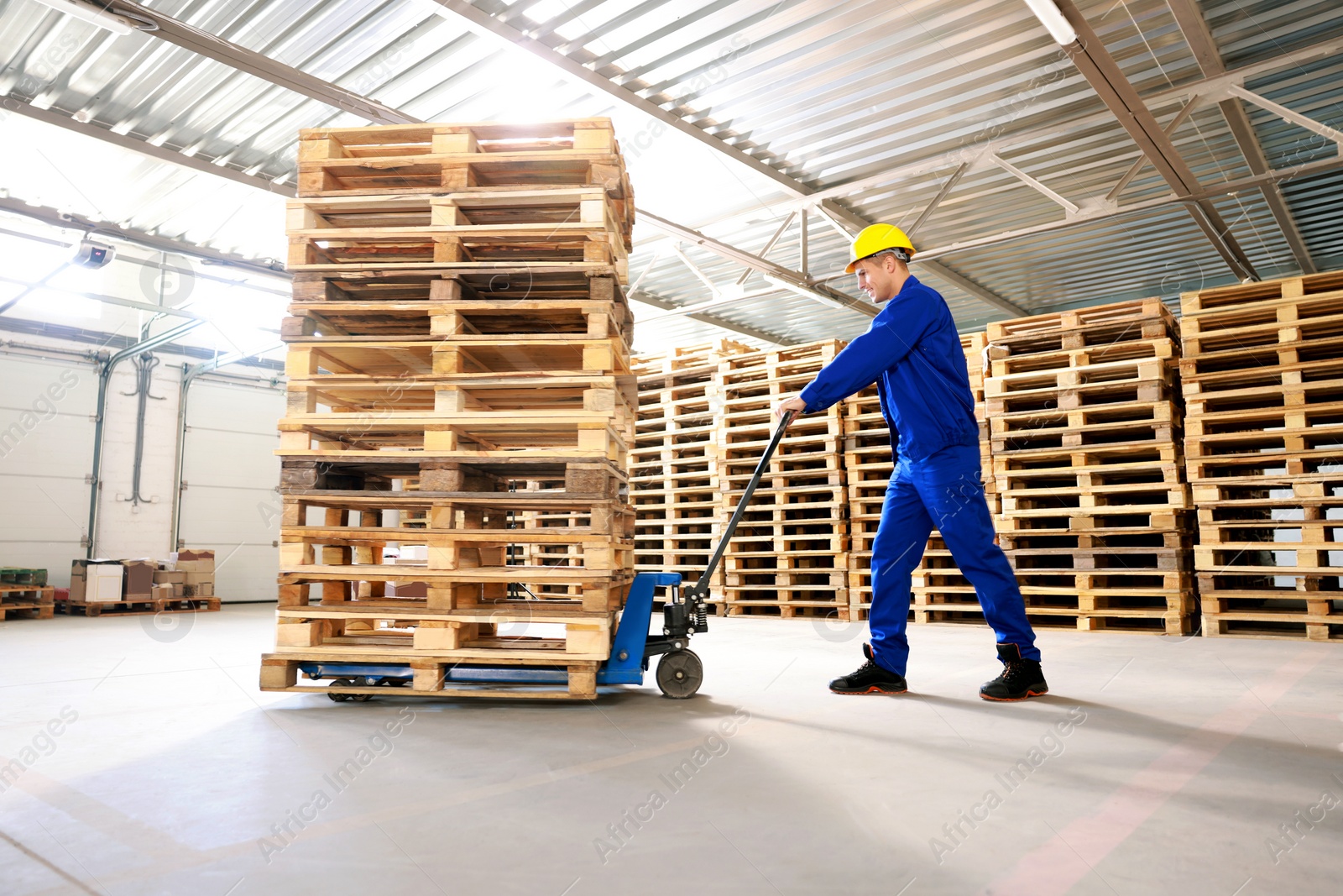 Image of Worker moving wooden pallets with manual forklift in warehouse