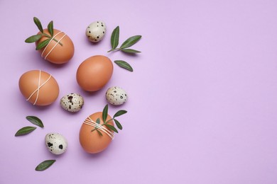 Beautifully decorated Easter eggs and green leaves on lilac background, flat lay. Space for text