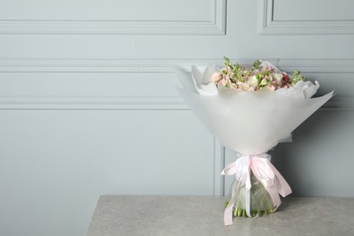 Photo of Beautiful bouquet of fresh flowers on table near grey wall, space for text