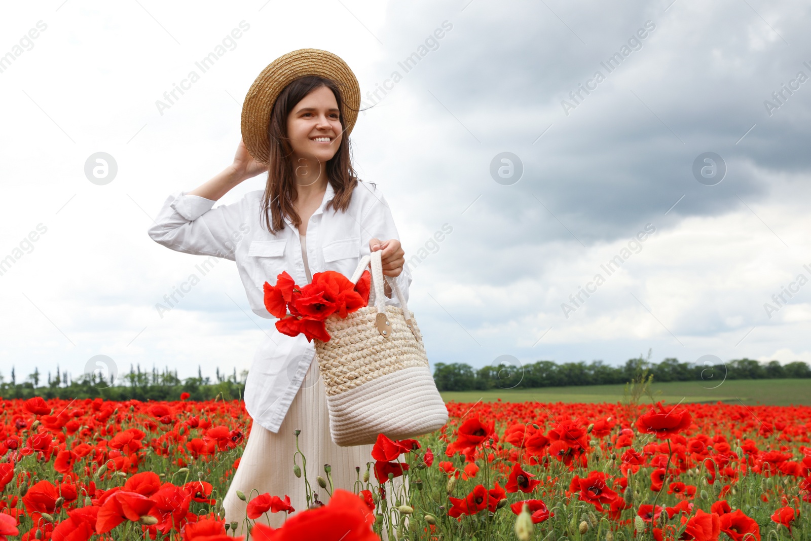 Photo of Woman holding handbag with poppy flowers in beautiful field