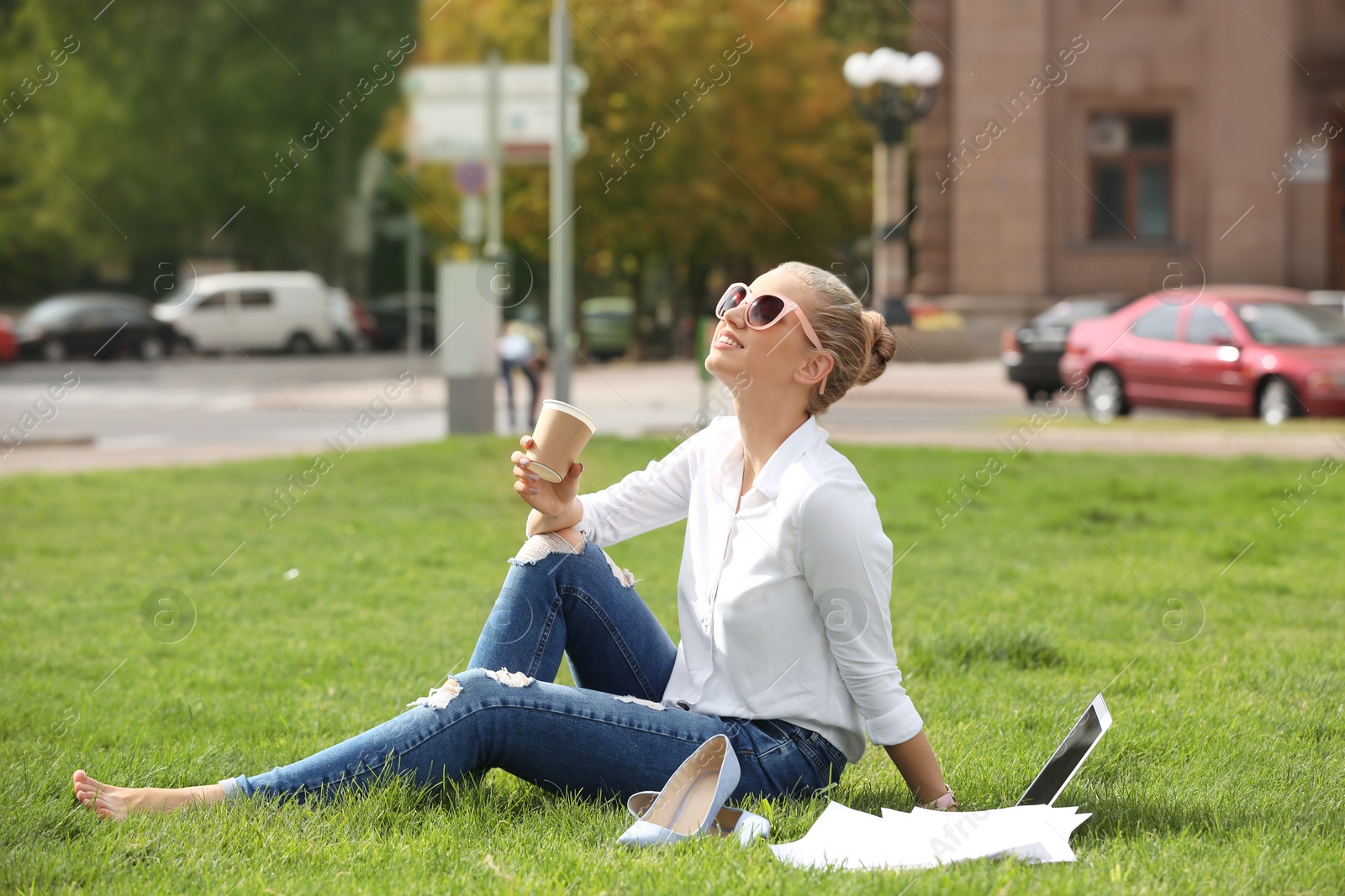 Photo of Young woman with cup of coffee sitting on green lawn in park. Joy in moment