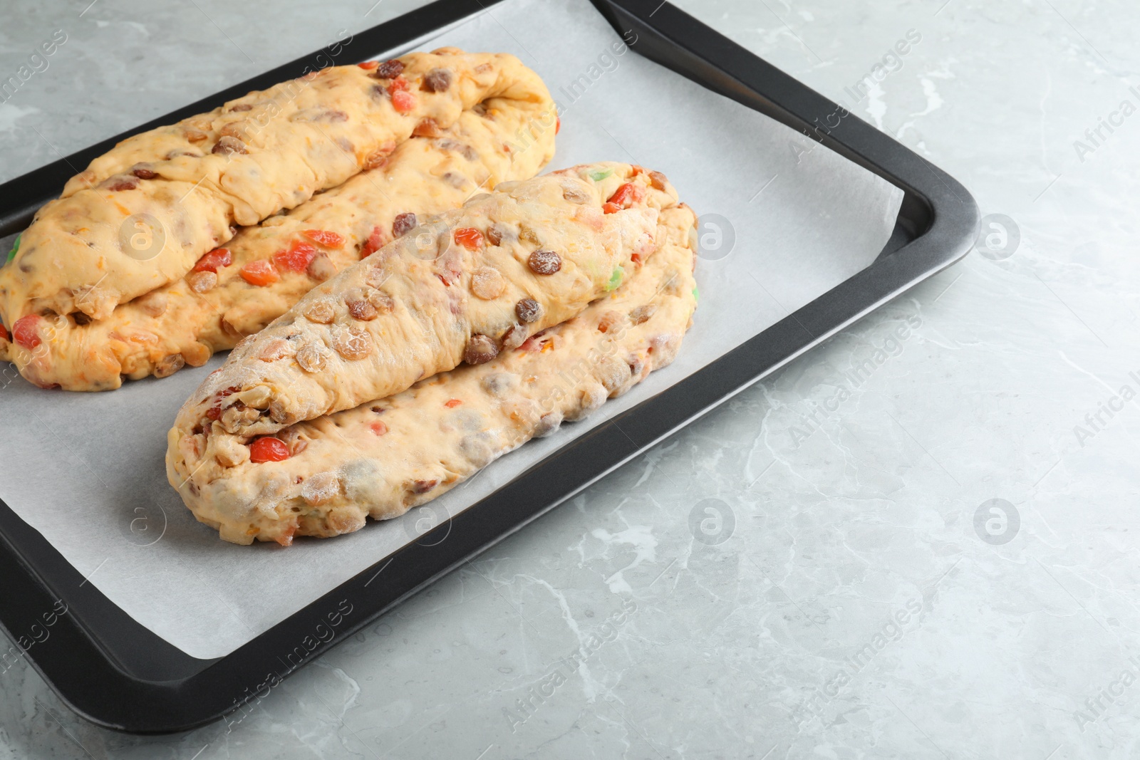 Photo of Baking tray with raw homemade Stollens on grey marble table, space for text. Traditional German Christmas bread