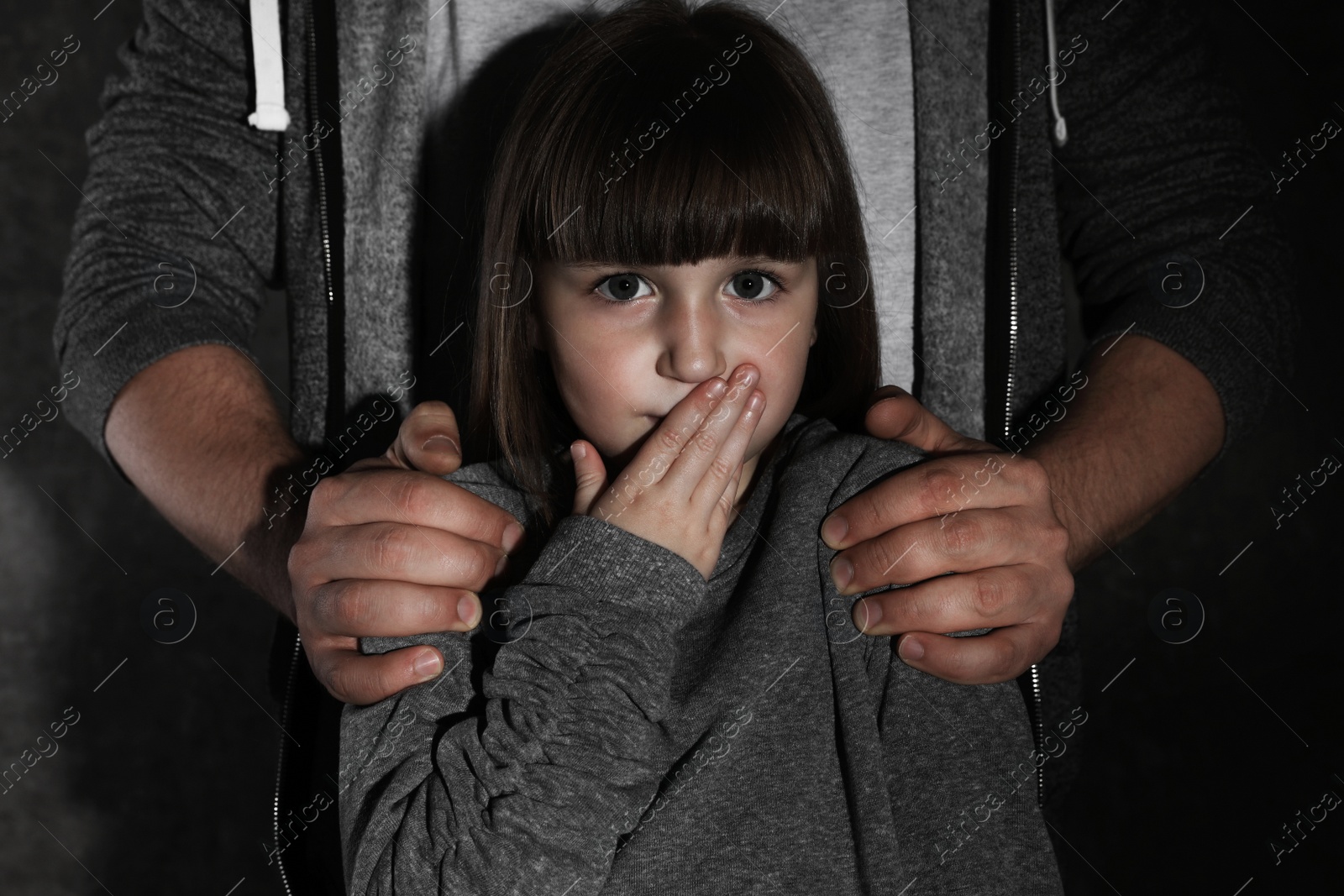 Photo of Scared little girl and adult man on dark background. Child in danger