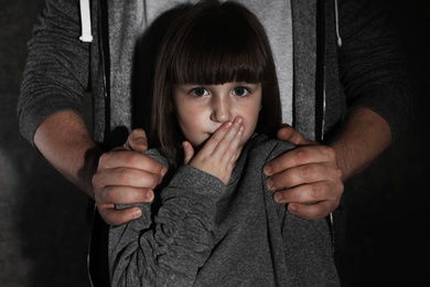 Photo of Scared little girl and adult man on dark background. Child in danger