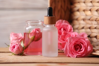 Photo of Bottles of essential rose oil and flowers on wooden table