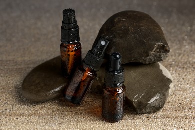Photo of Bottles of organic cosmetic products and stones on wet surface