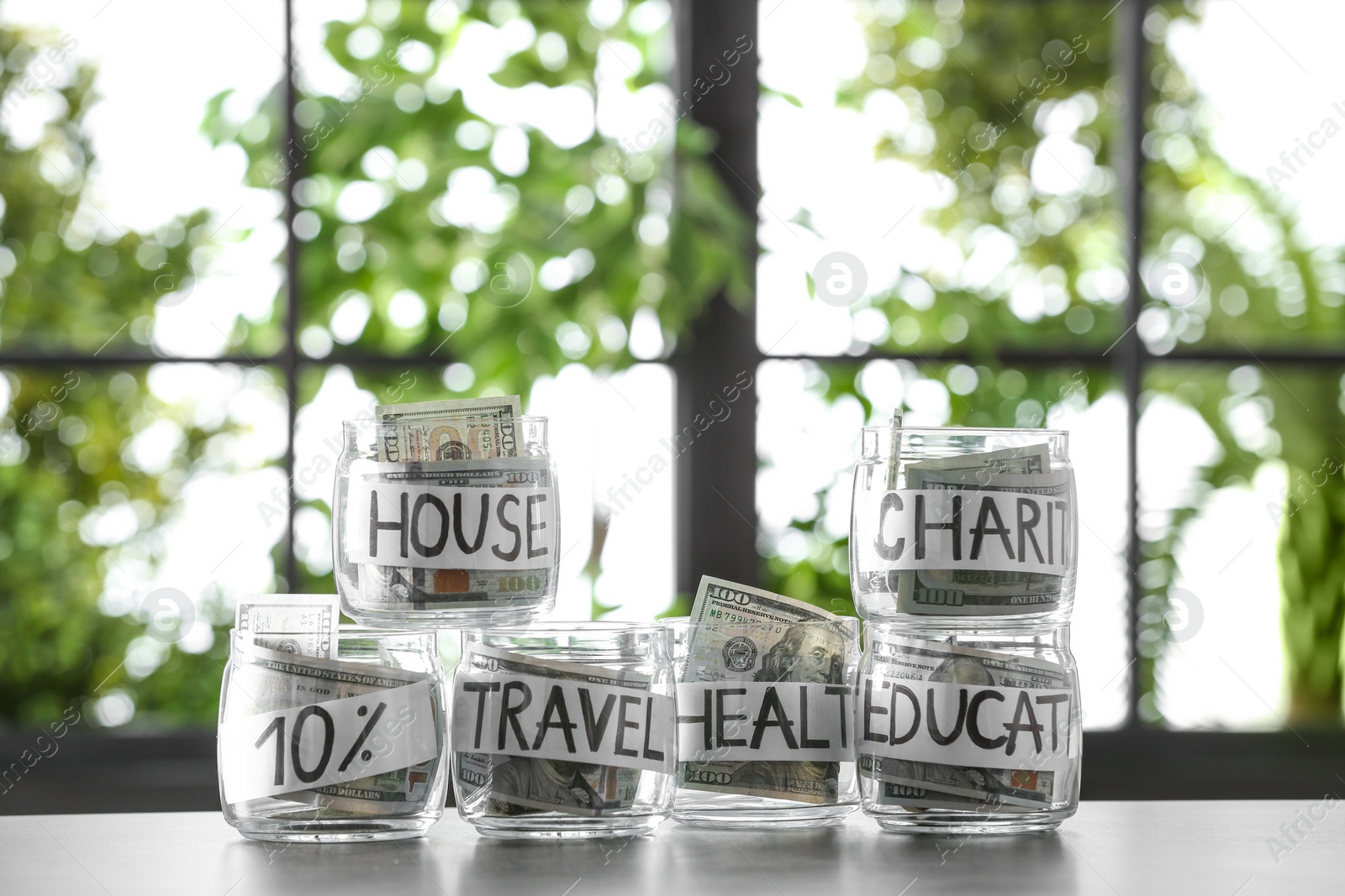 Photo of Glass jars with money for different needs on table against blurred background