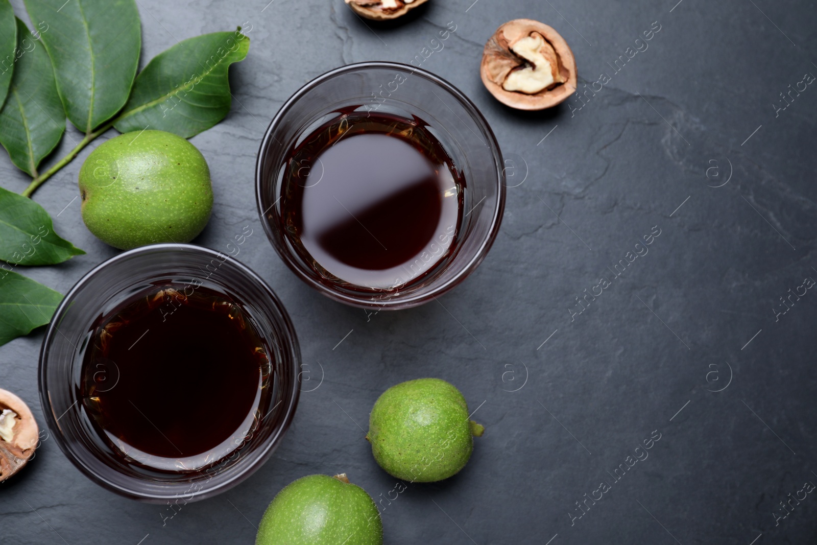 Photo of Delicious liqueur and fresh walnuts on black table, flat lay. Space for text