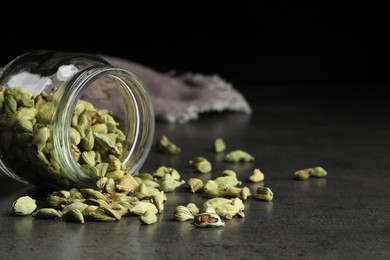 Jar with dry cardamom pods on dark grey table, space for text