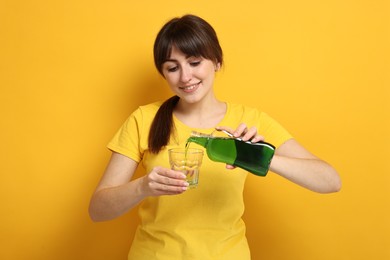 Young woman using mouthwash on yellow background