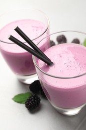 Delicious blackberry smoothie in glasses, fresh berries and mint on grey table, closeup