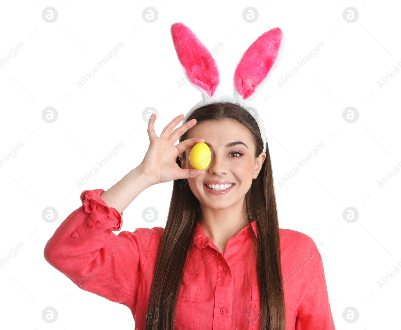 Photo of Beautiful woman in bunny ears headband holding Easter egg near eye on white background