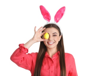 Photo of Beautiful woman in bunny ears headband holding Easter egg near eye on white background