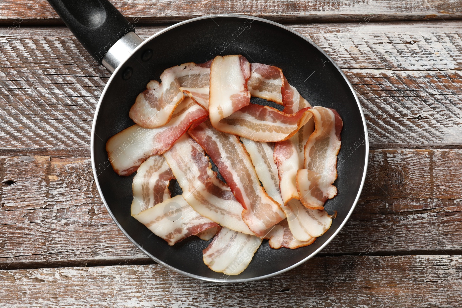 Photo of Delicious bacon slices in frying pan on wooden table, top view