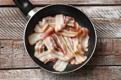 Delicious bacon slices in frying pan on wooden table, top view