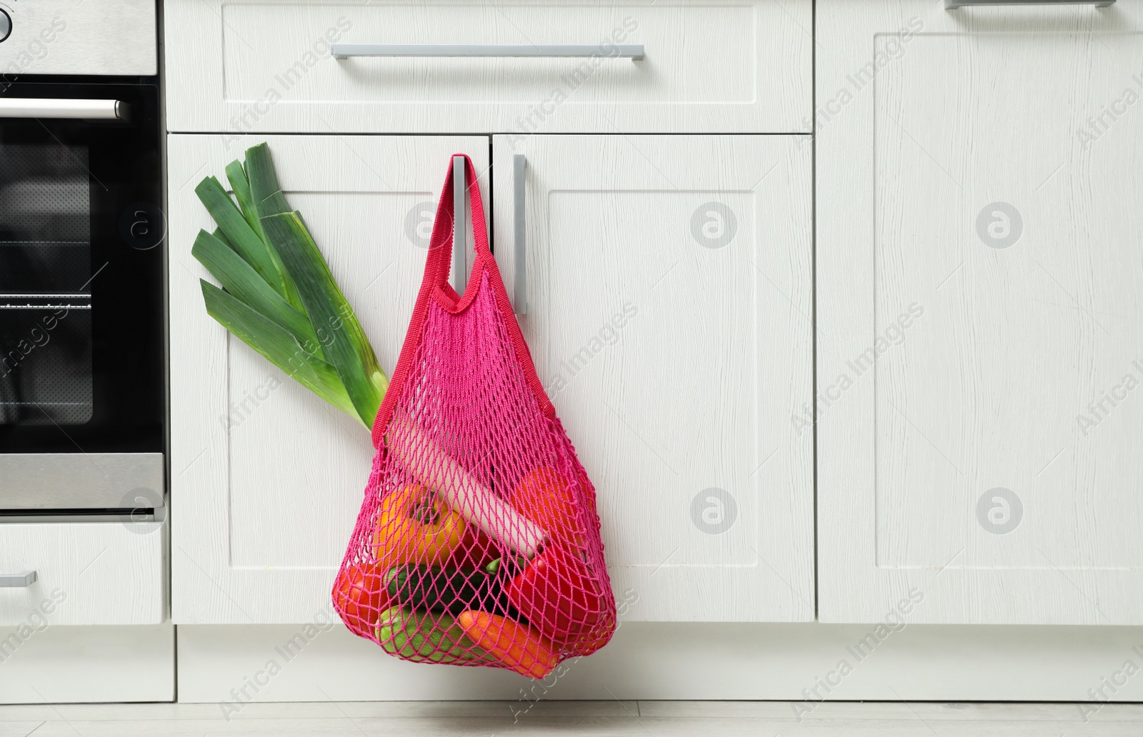 Photo of Net bag with vegetables hanging on cabinet door in kitchen