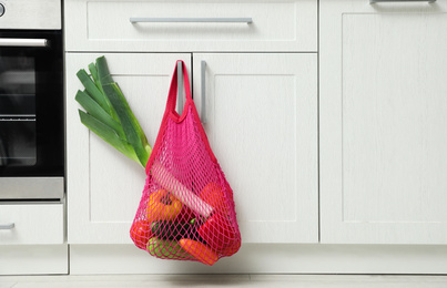 Net bag with vegetables hanging on cabinet door in kitchen