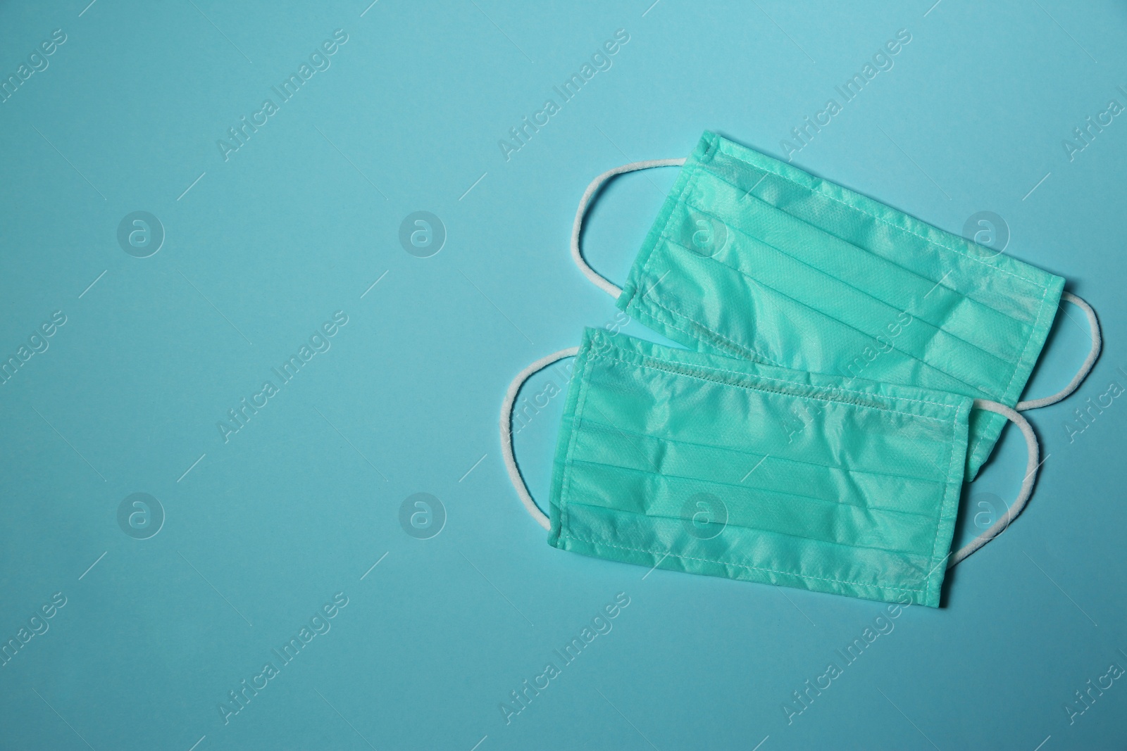 Photo of Disposable face masks on light blue background, flat lay with space for text. Protective measures during coronavirus quarantine