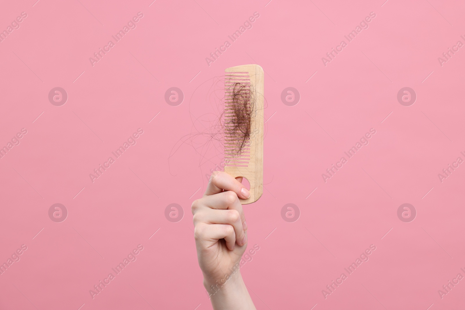 Photo of Woman holding comb with lost hair on pink background, closeup. Alopecia problem