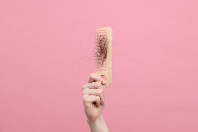Photo of Woman holding comb with lost hair on pink background, closeup. Alopecia problem