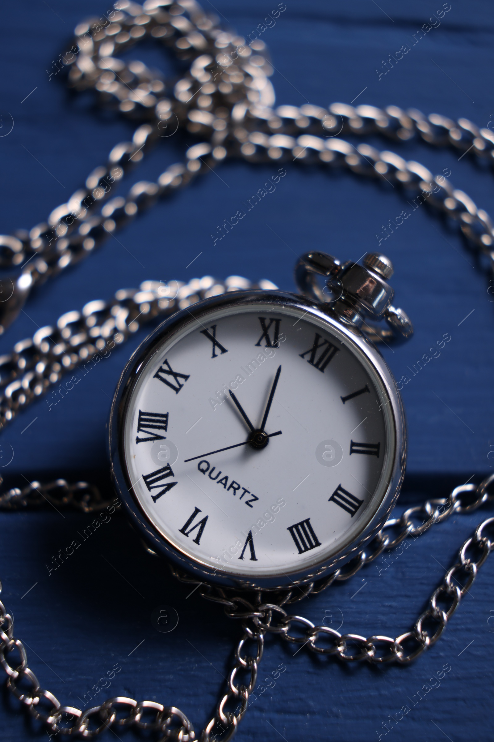 Photo of Silver pocket clock with chain on blue wooden table, closeup