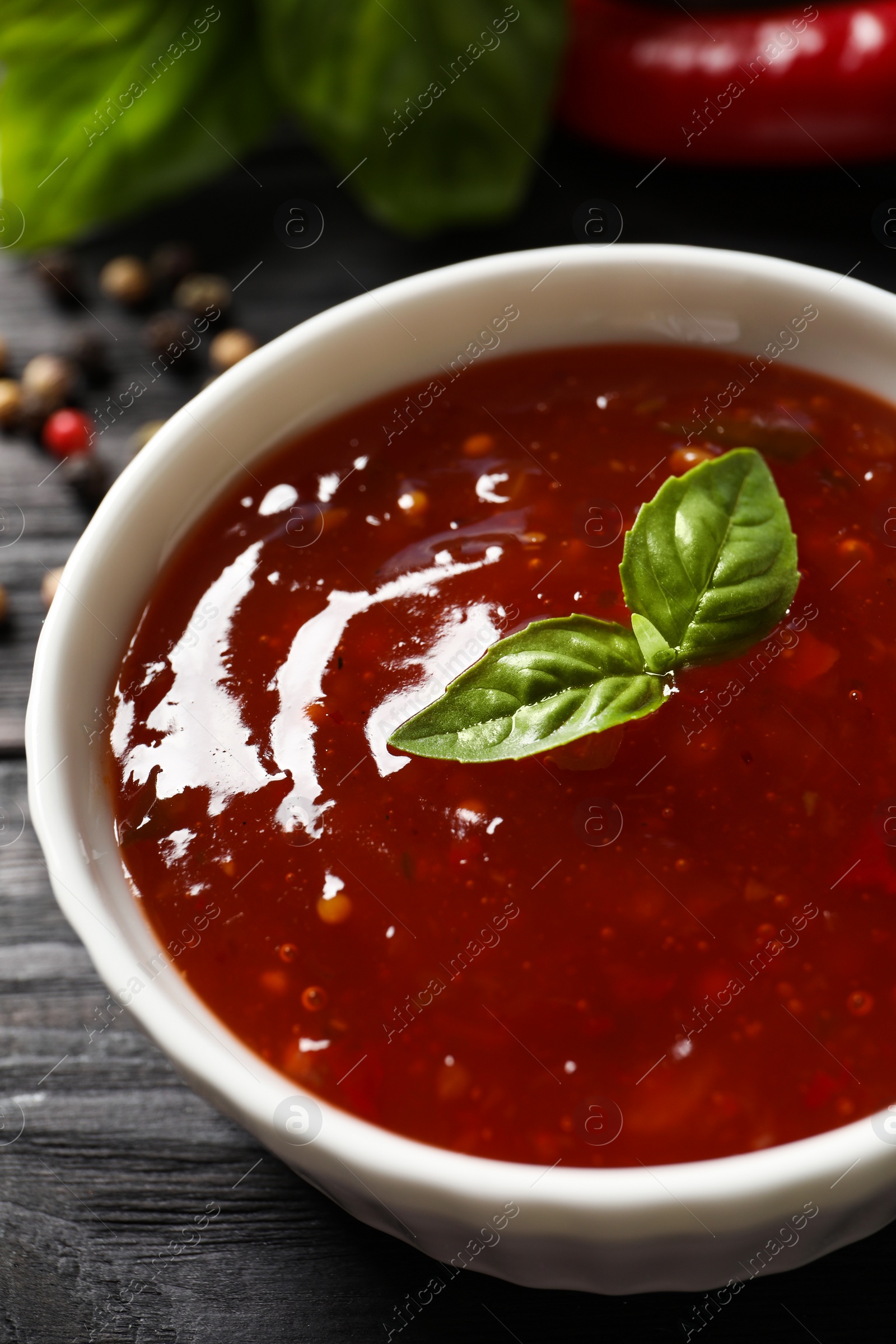 Photo of Spicy chili sauce with basil on dark wooden table, closeup