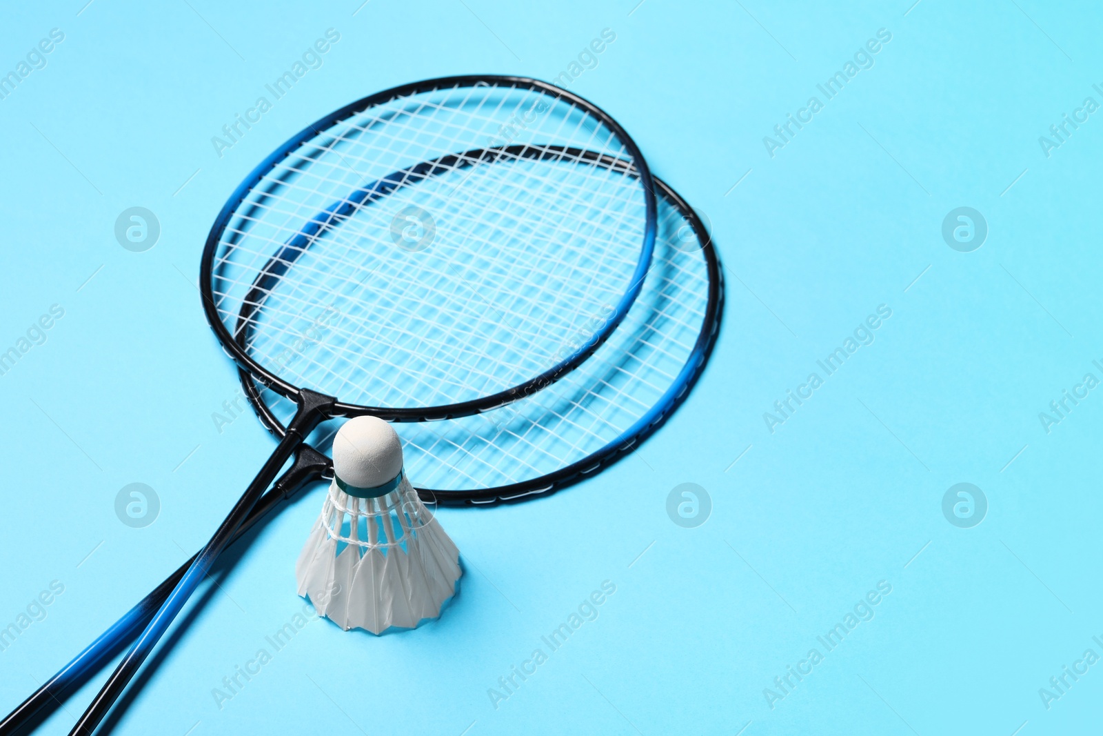 Photo of Feather badminton shuttlecocks and rackets on light blue background, space for text