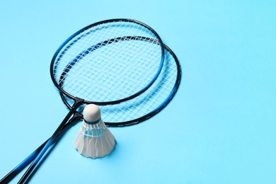 Feather badminton shuttlecocks and rackets on light blue background, space for text